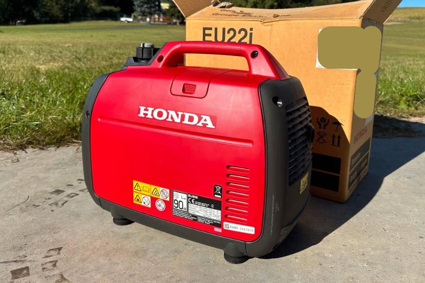 Der Honda EU 22i Notstromaggregat steht auf dem Boden vor einer Wiese.